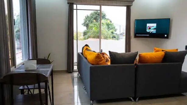 A modern living room with a grey sofa, a dining table with chairs, and a TV mounted on the wall. - Modern Apartment in La Ceiba ‼️No Cleaning Fee‼️ (La Ceiba)