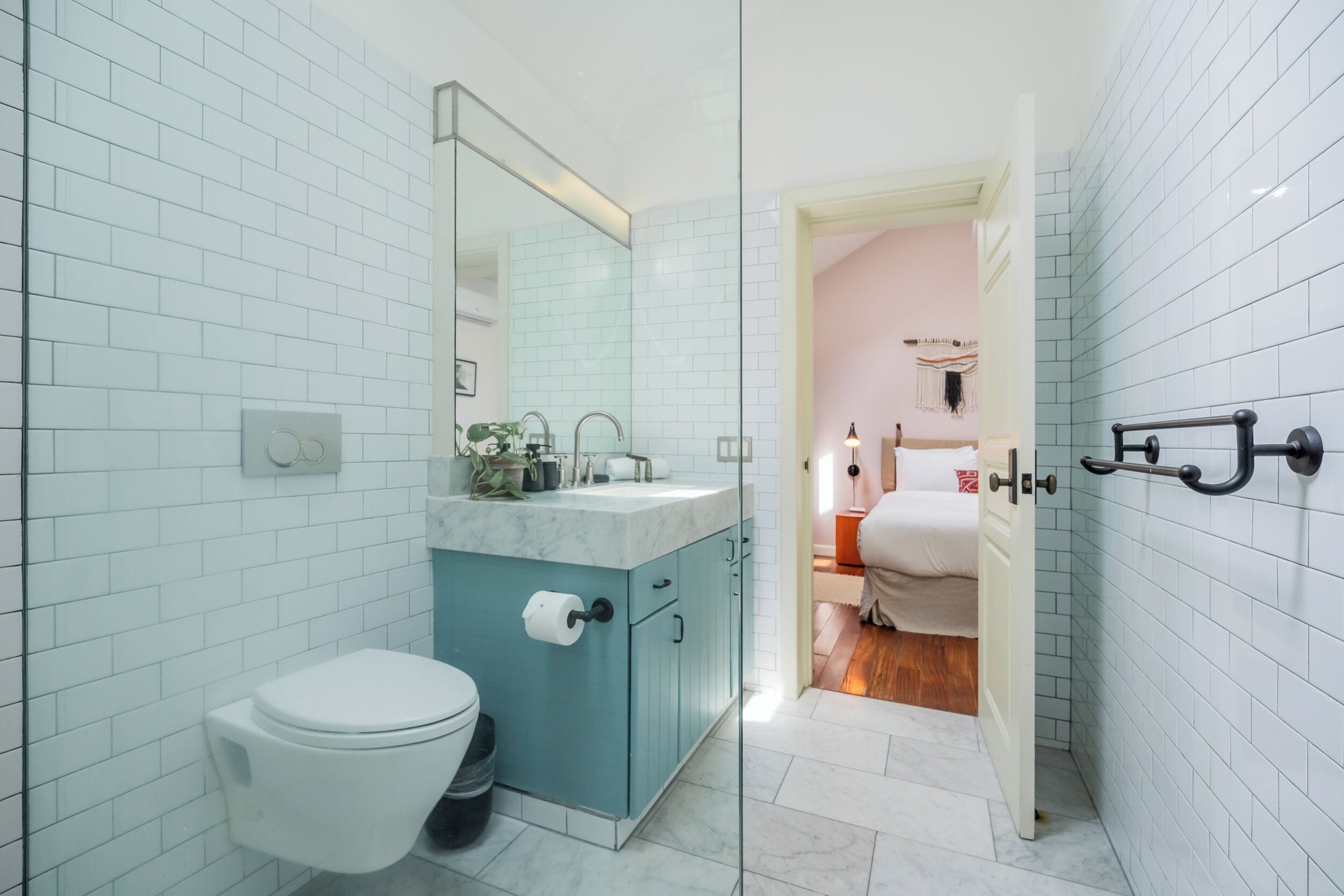 A bathroom with white tiled walls, a marble sink, a toilet, and a glass shower enclosure.