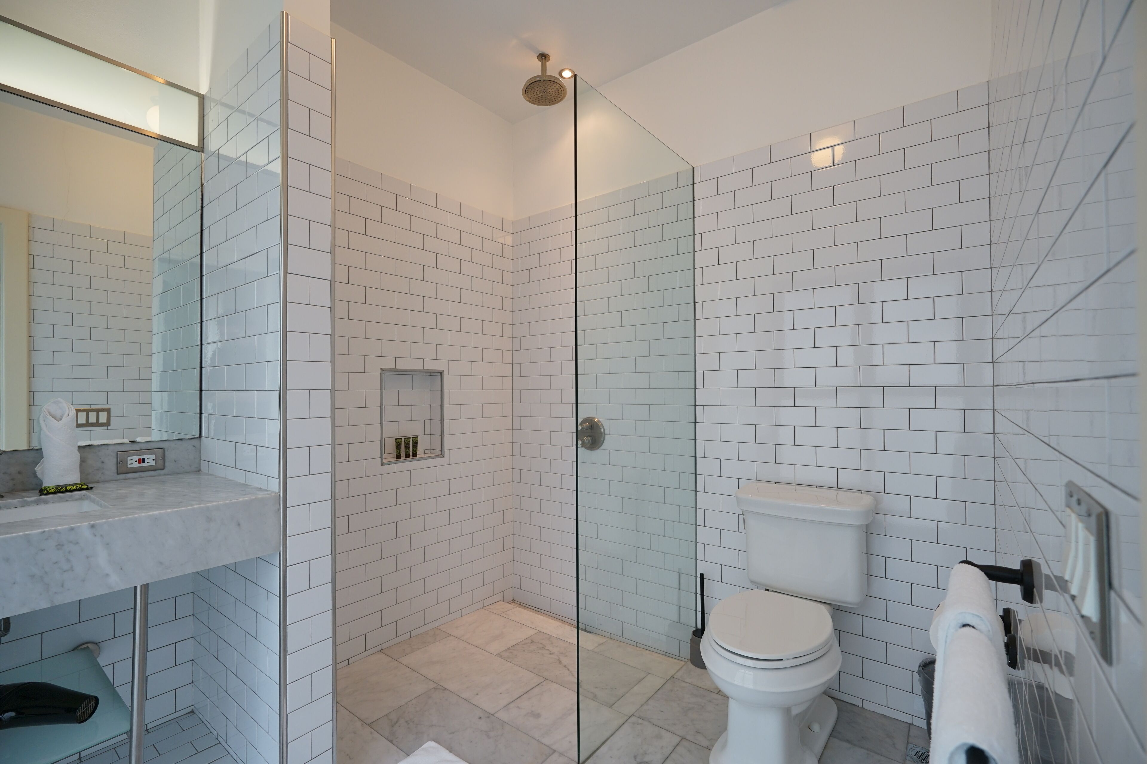 A modern bathroom with white subway tiles, a glass shower enclosure, a white toilet, and a marble sink.