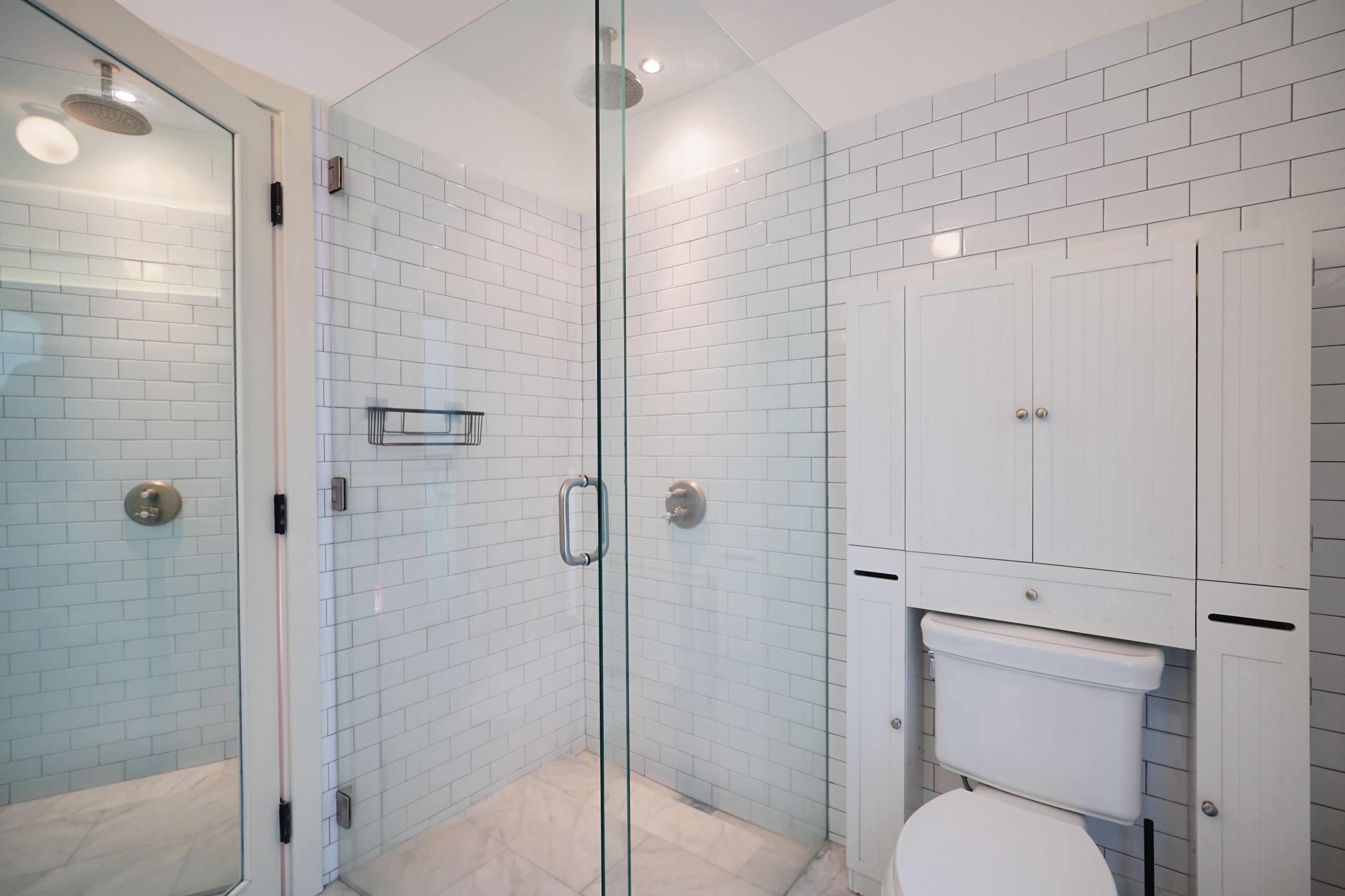 A modern bathroom with a glass-enclosed shower, white tiled walls, and a white toilet.