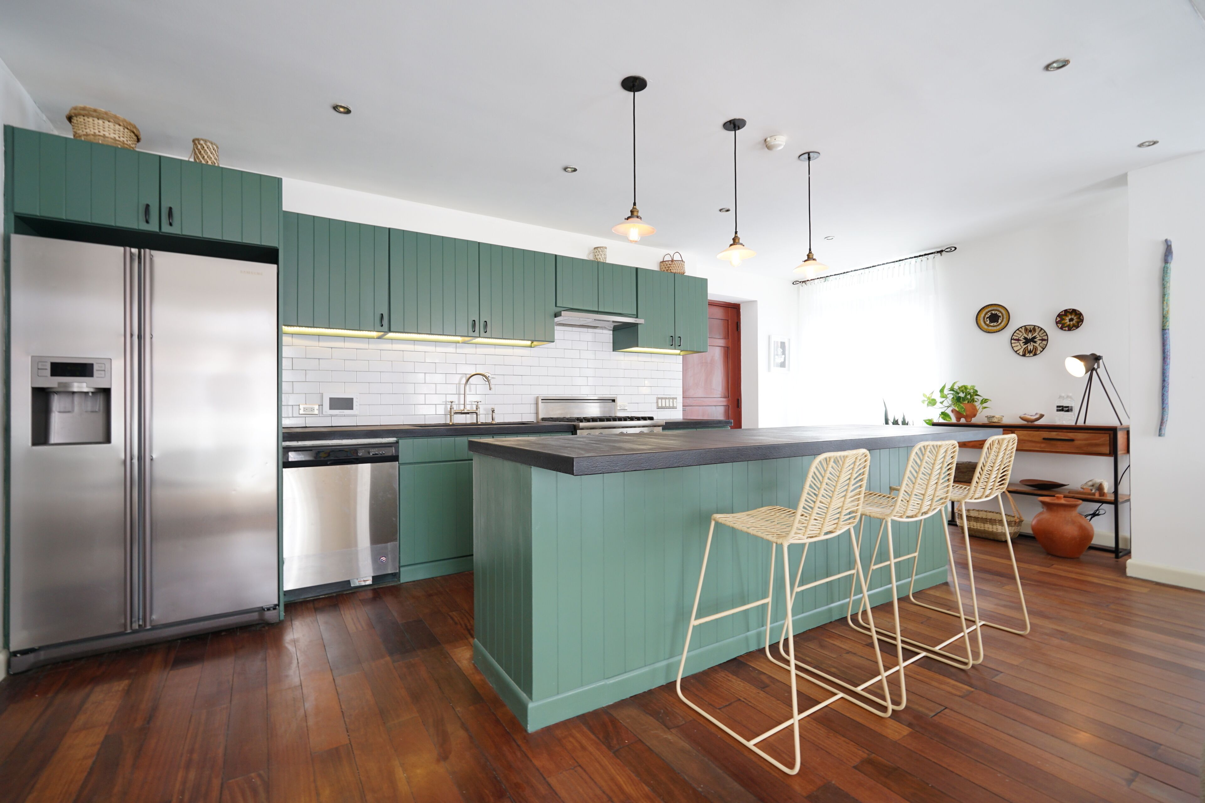 A modern kitchen with green cabinets, stainless steel appliances, and a central island with bar stools.