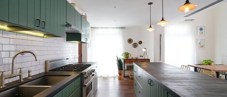 A modern kitchen with green cabinets, a stainless steel sink, and a wooden countertop.