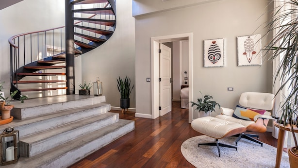A modern interior with a spiral staircase, hardwood flooring, a white armchair, and decorative wall art.