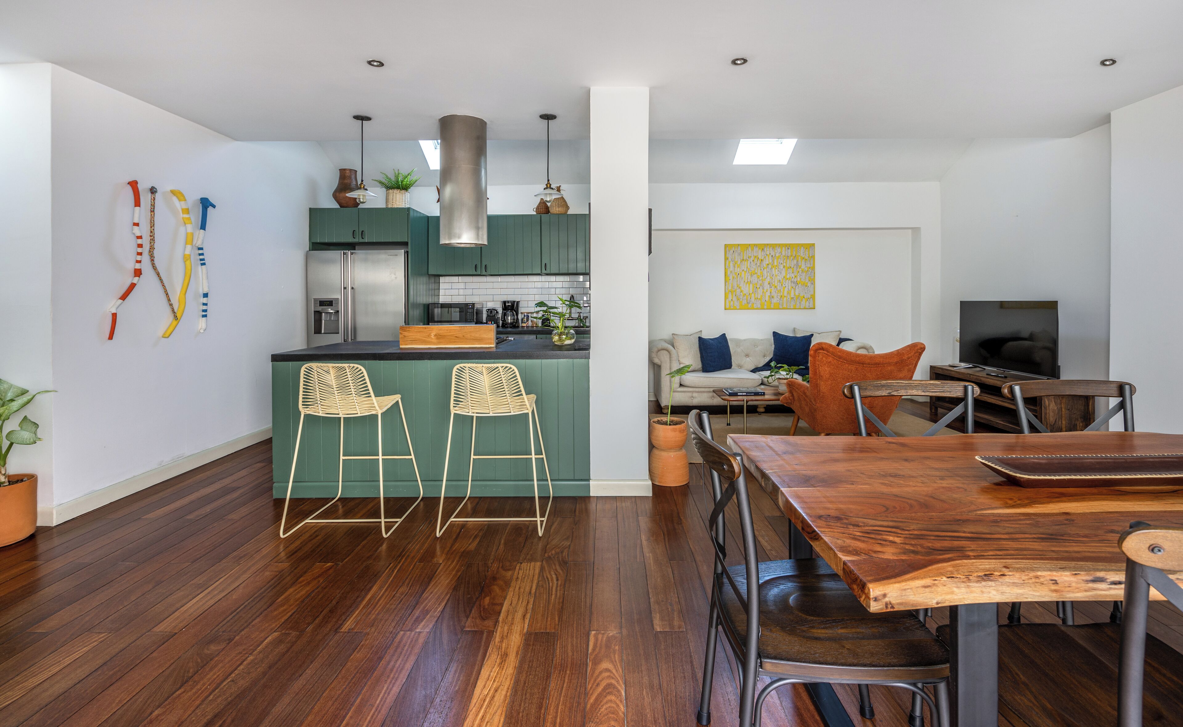 A modern kitchen with green cabinets, a central island with bar stools, and a dining area with a wooden table and chairs.