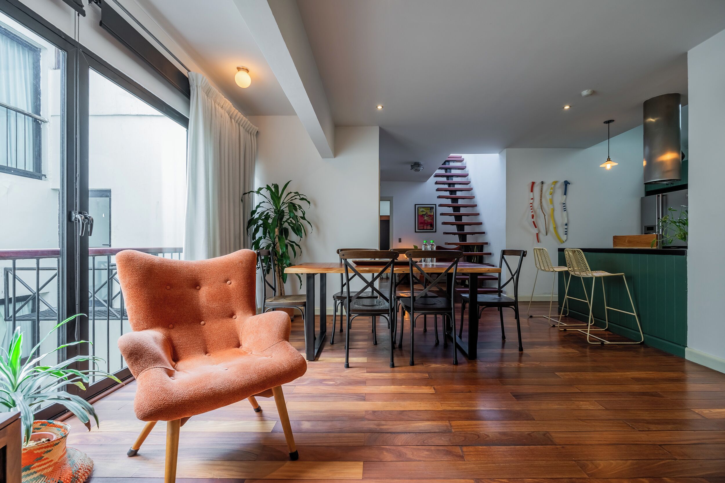 A spacious living area with a wooden floor, a dining table with chairs, a staircase, and a kitchen area.
