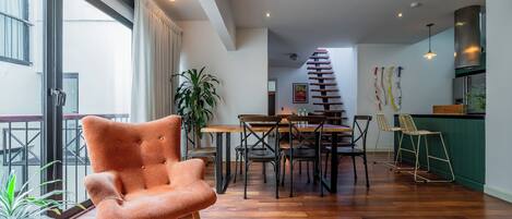 A spacious living area with a wooden floor, a dining table with chairs, a staircase, and a kitchen area.