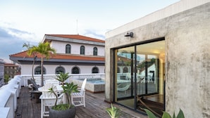 A rooftop deck with outdoor seating, a hot tub, and a view of a historic building with a tiled roof.