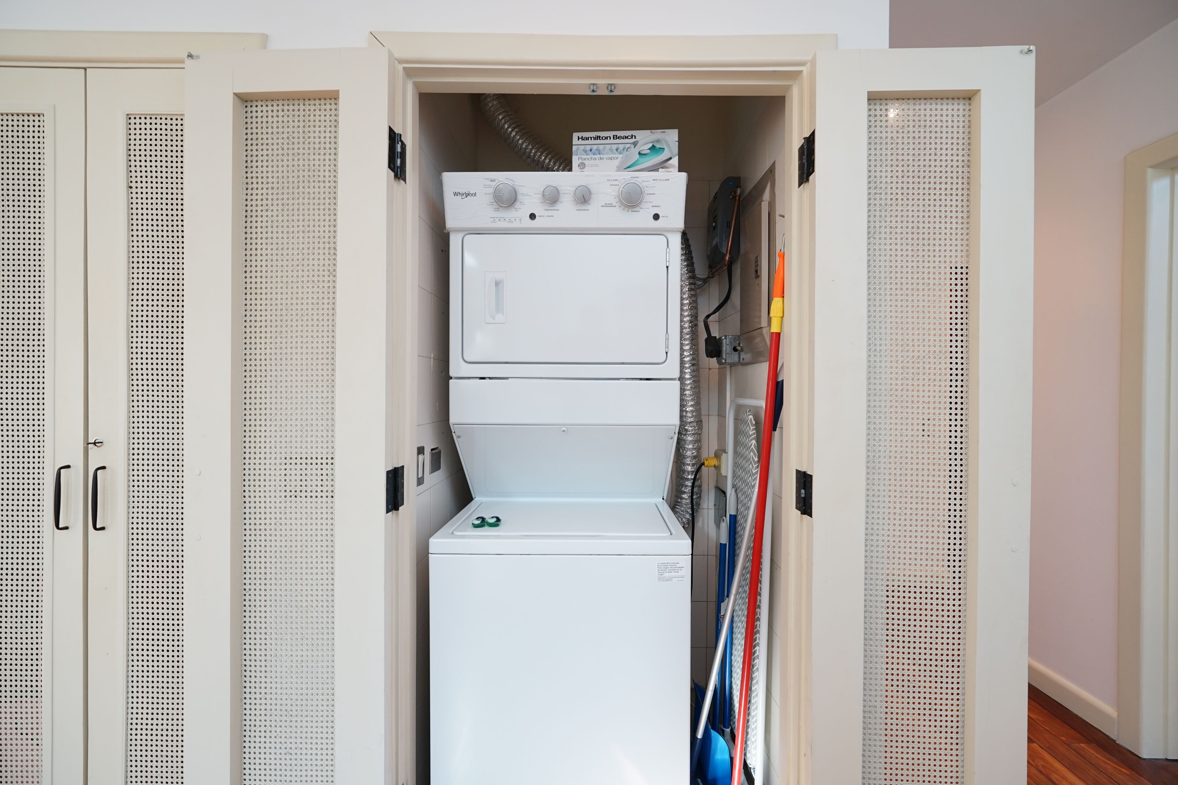 A compact laundry room with a front-loading washer and dryer, a sign for Hamilton Beach brand appliances, and a mop leaning against the wall.
