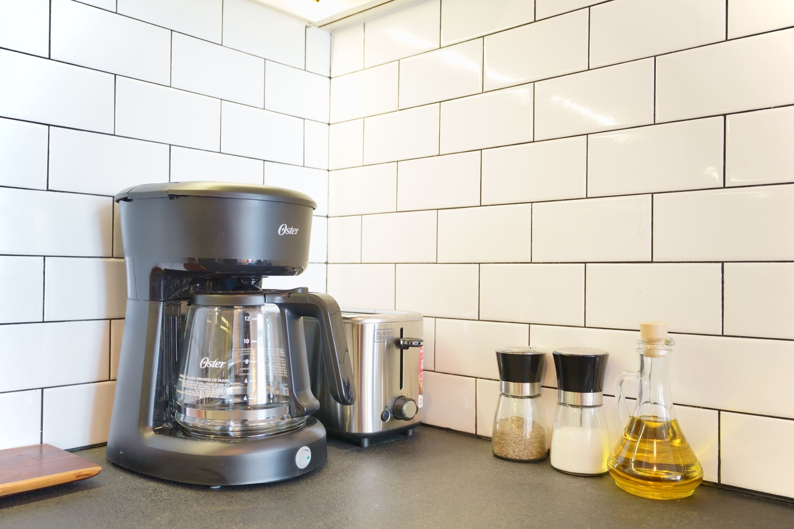 A kitchen with a coffee maker, toaster, salt and pepper shakers, and a bottle of oil on the counter.