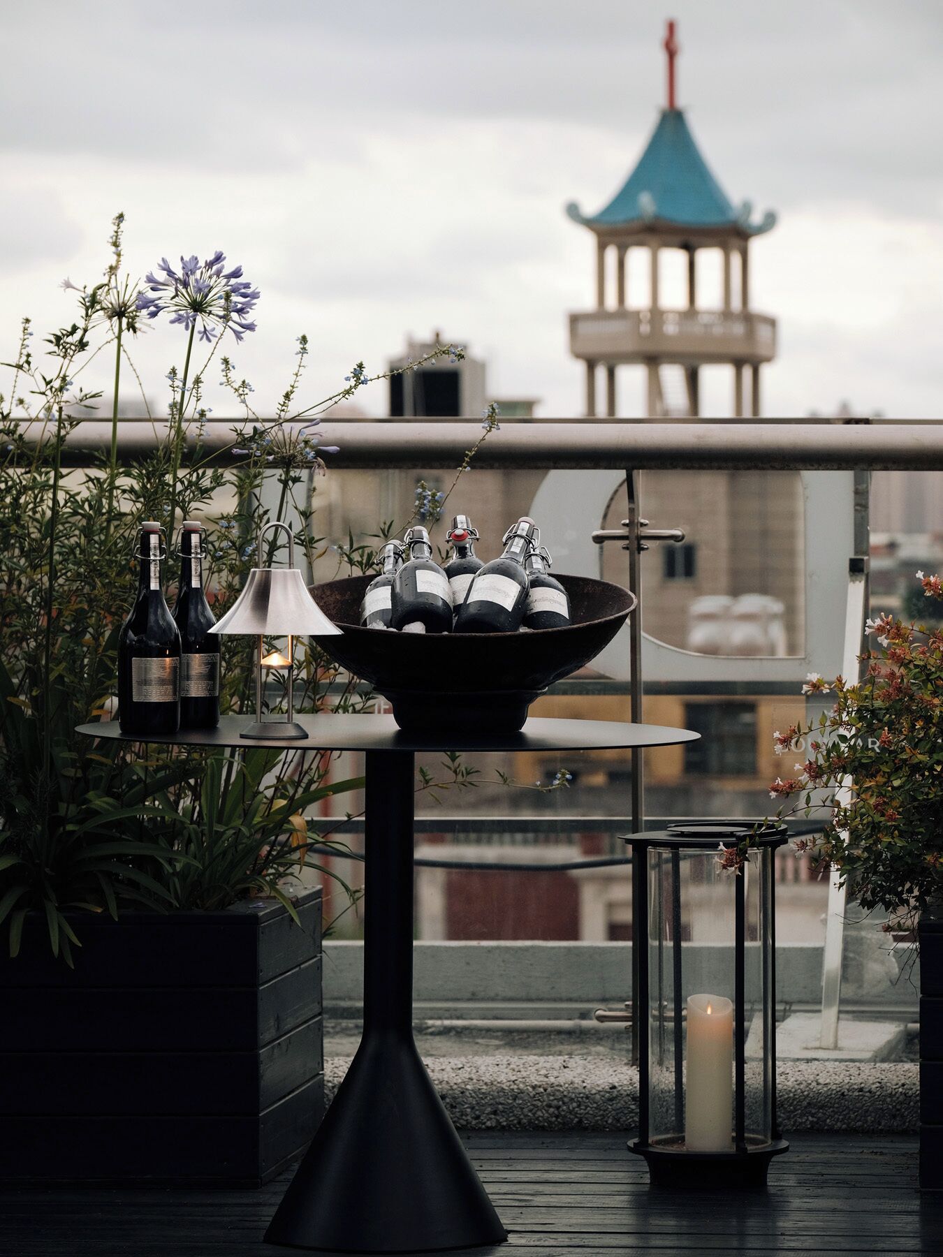 Una terraza en la azotea con una mesa que sostiene botellas de vino, una vela y un farol.