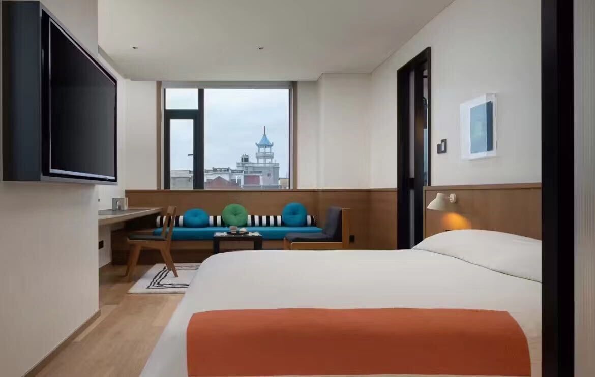 A hotel room with a bed, a desk, a chair, a sofa, a TV, and a window with a view of a tower.