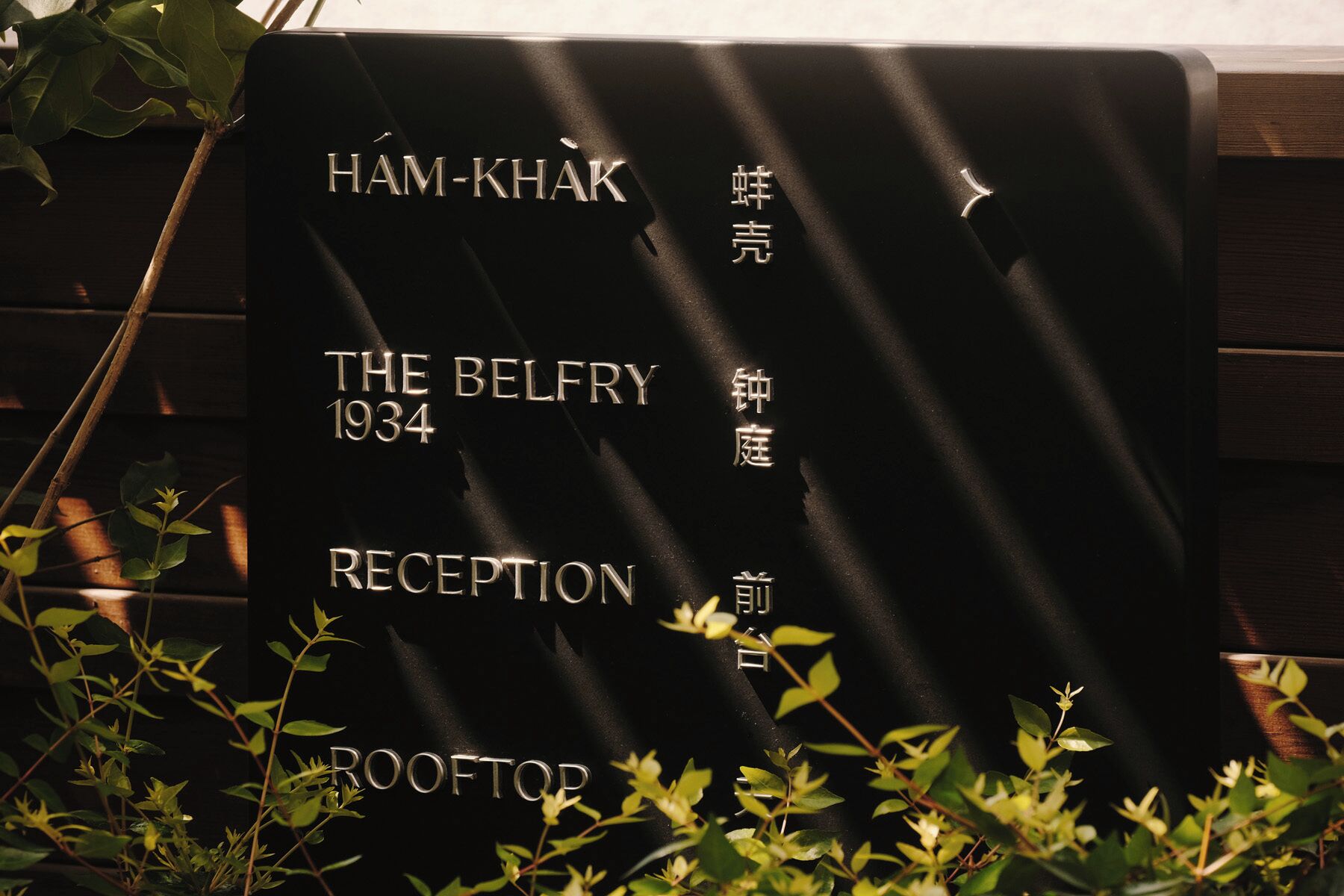 Ein Schild mit dem Schriftzug 'HAM-KHAK' und 'THE BELFRY 1934 RECEPTION ROOFTOP', umgeben von Grünpflanzen.