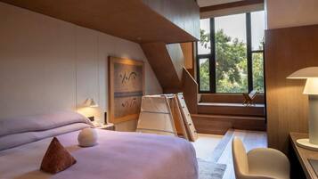 Una habitación de hotel moderna con una cama grande, un escritorio y una silla. Se ve una ventana con vistas a árboles y una escalera.