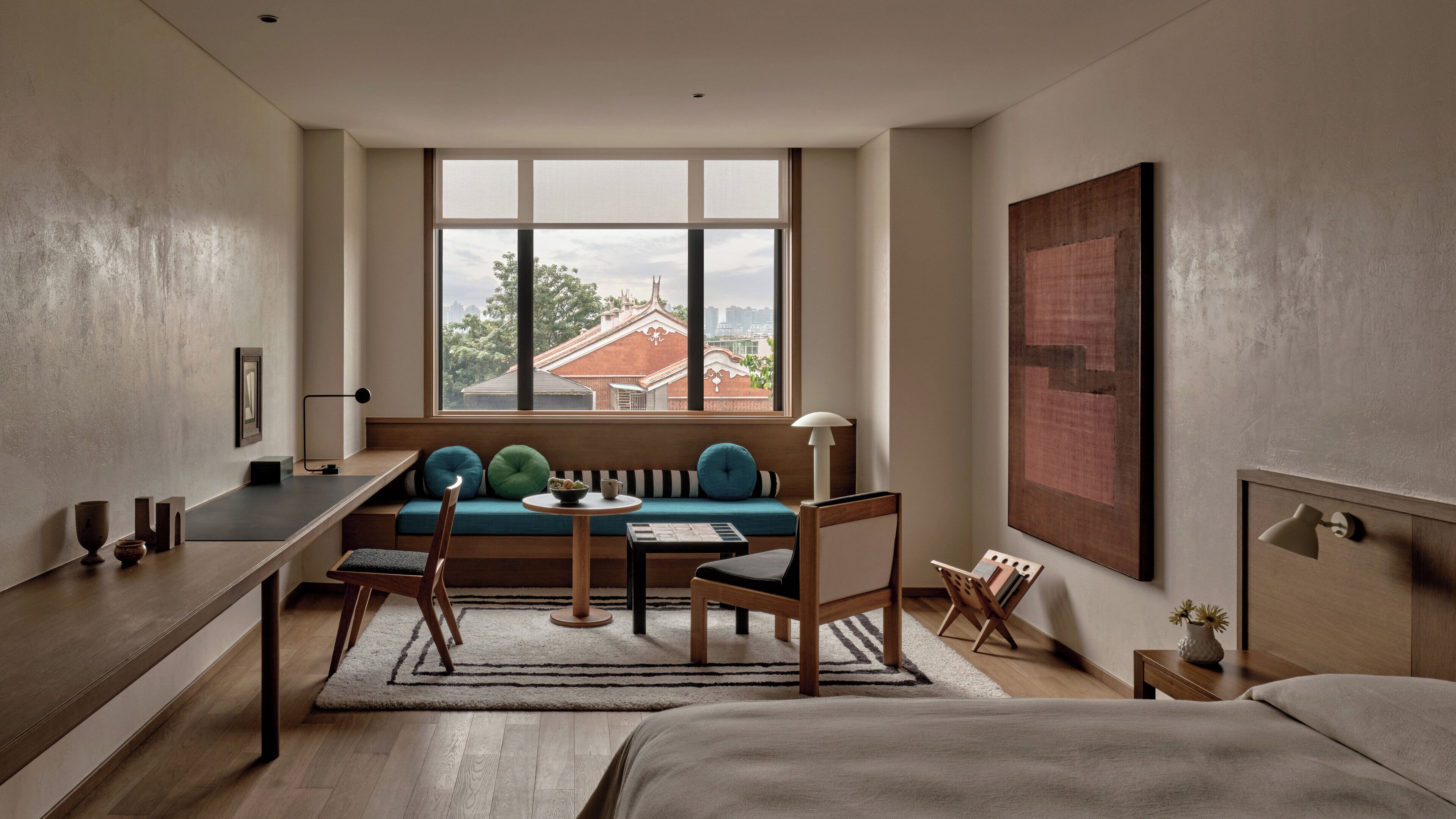 A modern hotel room with a large window, a sofa, a desk, and a bed.