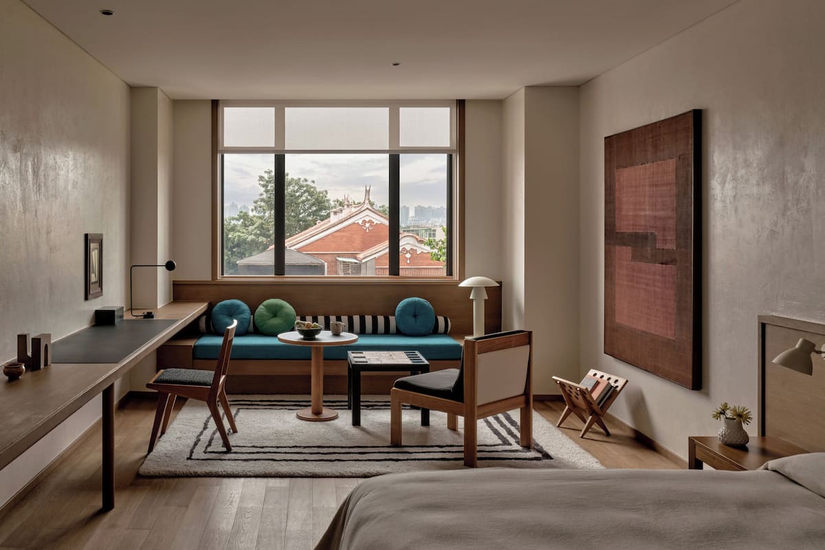 Moderni hotellihuone, jossa on suuri ikkuna, sohva, työpöytä ja sänky.