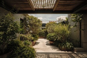 A covered outdoor space with a gravel path, surrounded by dense greenery and potted plants. - KAIPUU BELFRY (Quanzhou)