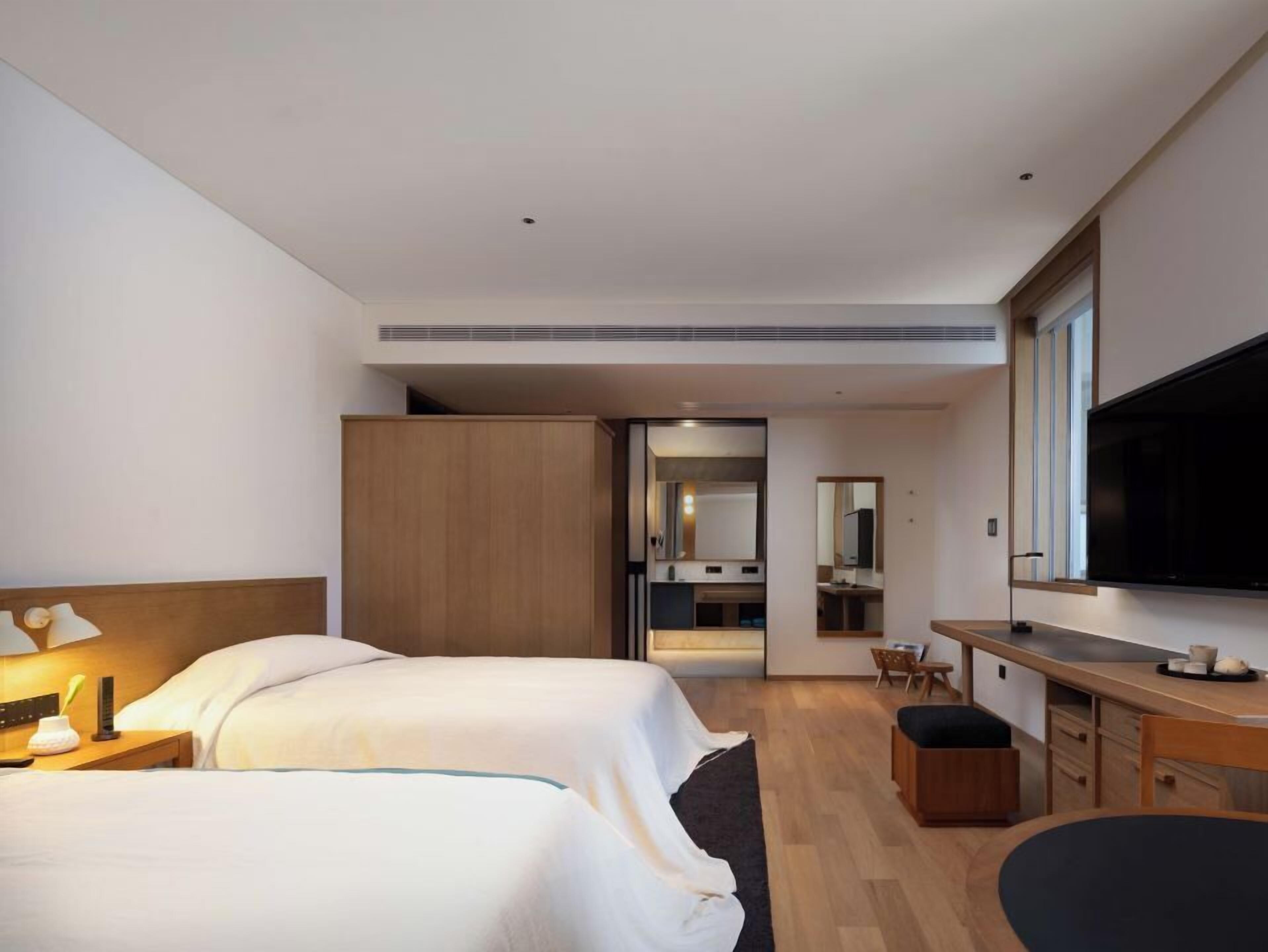 A hotel room with two beds, a desk, a TV, and a mirror.