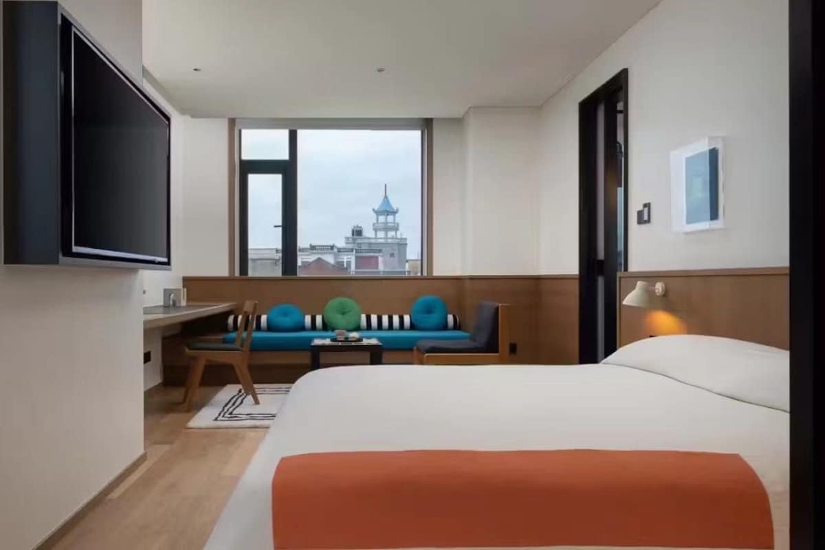 Habitación de hotel con cama, escritorio, silla, sofá, televisor y ventana con vista a una torre.