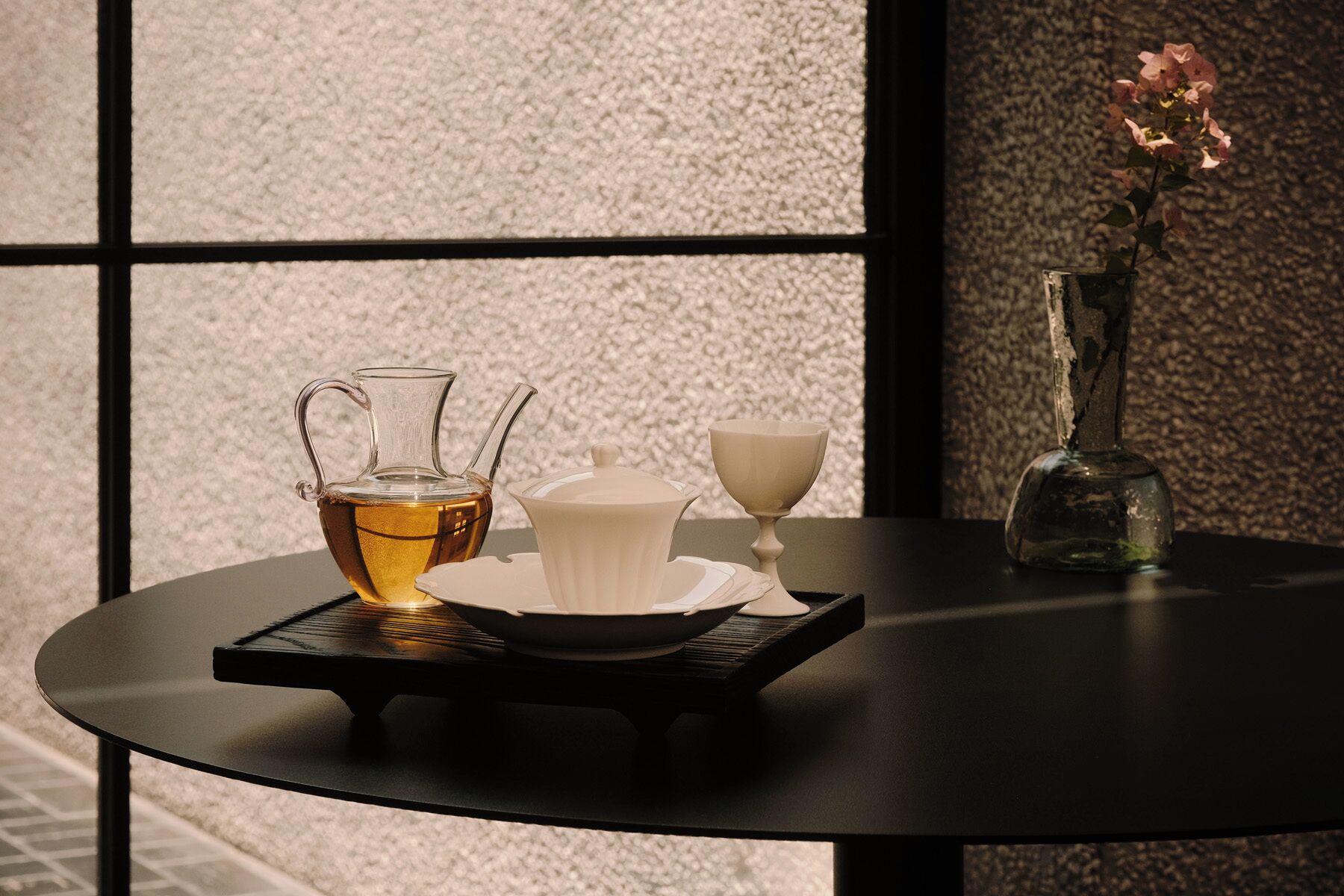 A table with a pitcher of tea, a white cup, and a vase with flowers.
