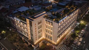 A multi-story hotel with a rooftop garden, a prominent entrance, and a well-lit facade.