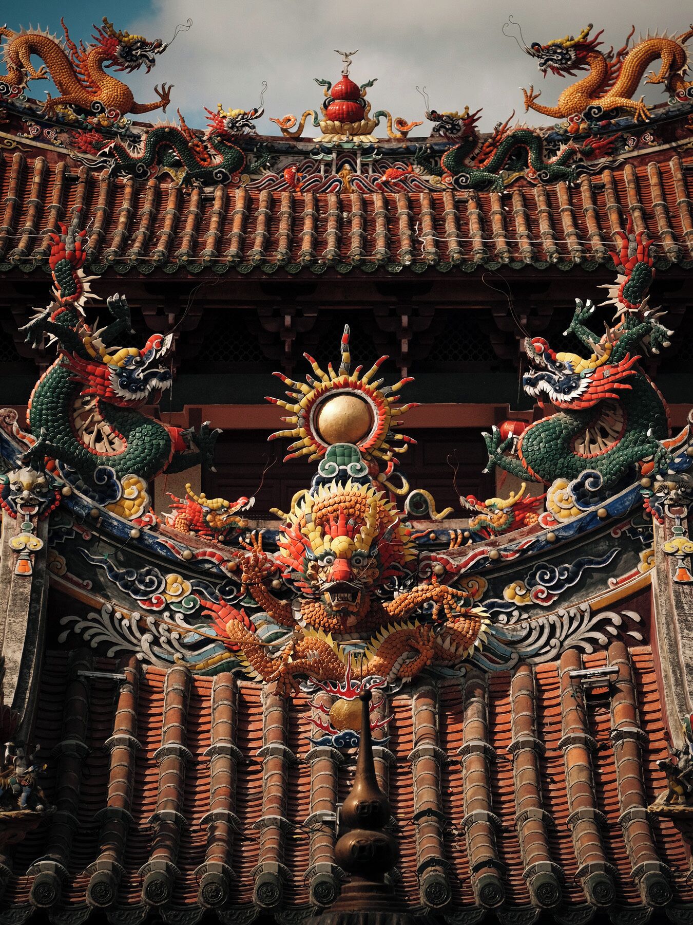 Tejado chino tradicional con elaboradas decoraciones de dragones y una esfera dorada central.