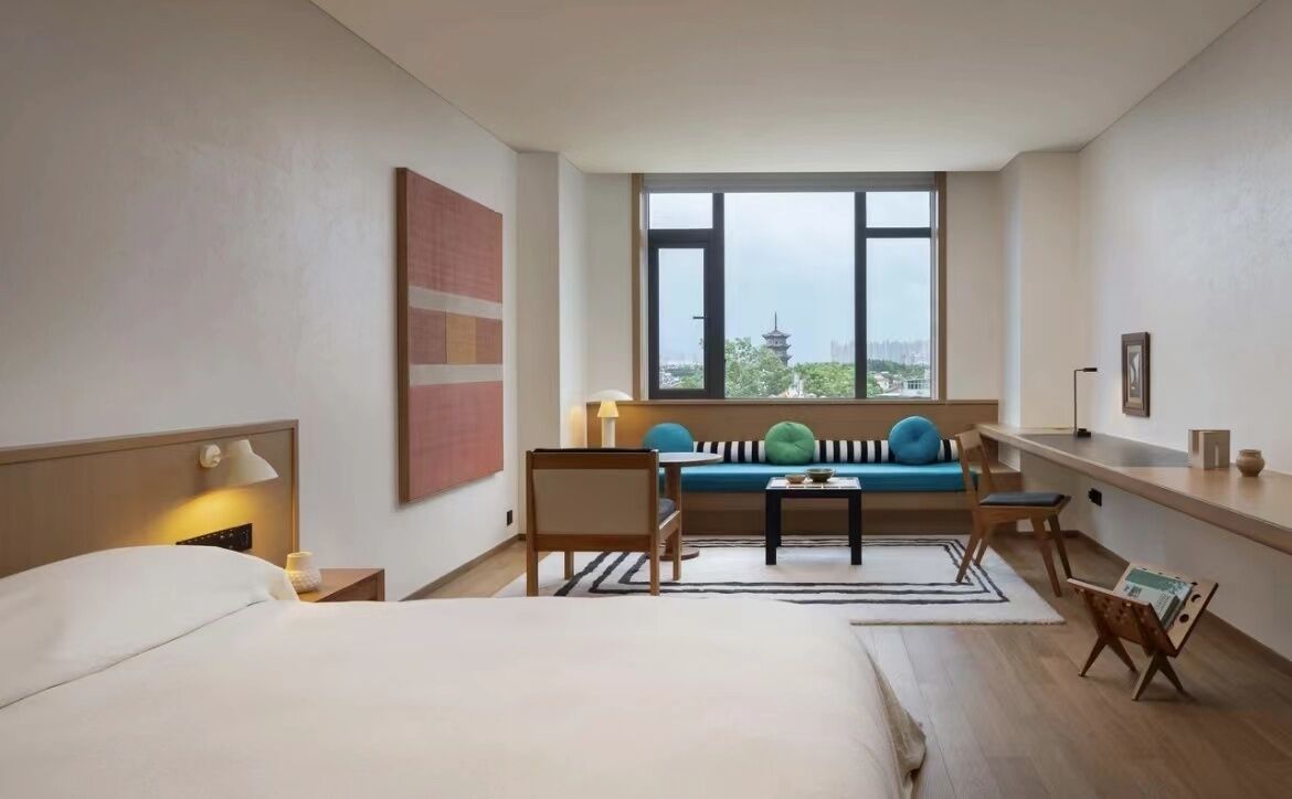 A hotel room with a bed, a sofa, a desk, and a view of a tower through a large window.