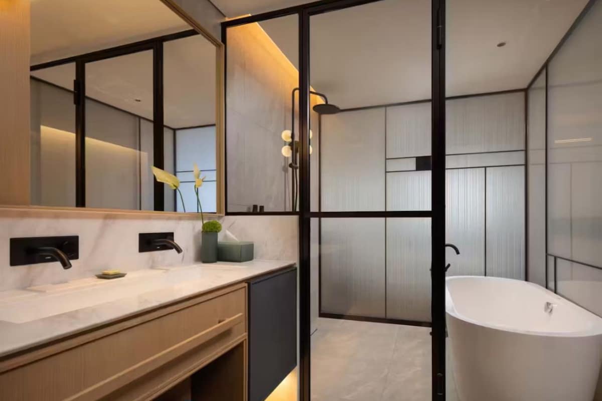 Un baño moderno con un espejo grande, dos lavamanos, una bañera y un box de ducha.