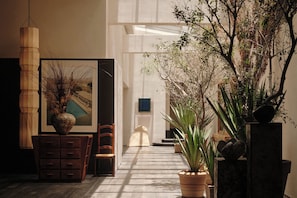A hallway with a wooden dresser, a chair, a framed picture, and potted plants. - KAIPUU BELFRY (Quanzhou)