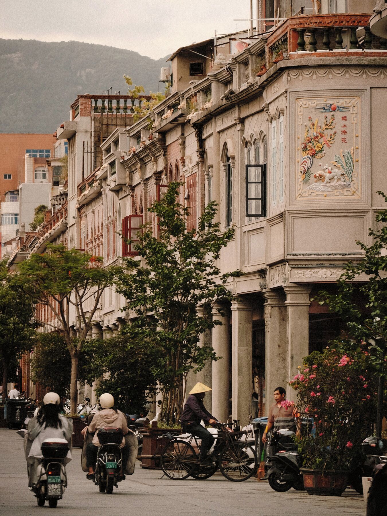 Un carrer amb edificis, una bicicleta i una persona conduint un patinet.