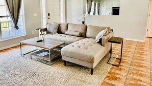 Ein modernes Wohnzimmer mit einem Ecksofa, einem Couchtisch und einem kleinen Beistelltisch.