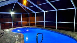 Ein Außenpool mit überdachtem Bereich, einer Metallleiter und einer Pflasterterrasse.