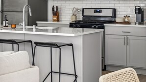 Een moderne keuken met witte kasten, een roestvrijstalen koelkast, een magnetron, een fornuis en een hangende lamp.