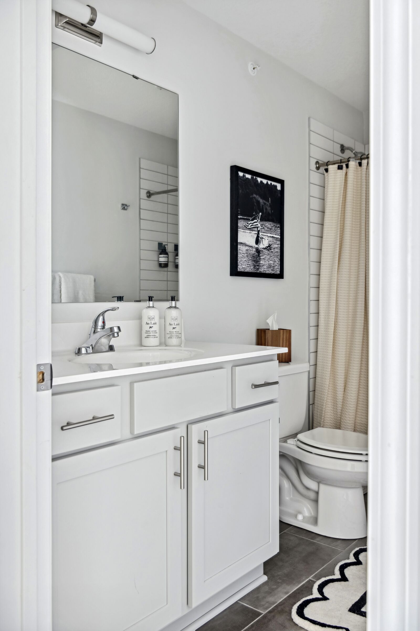 Et moderne badeværelse med et hvidt toiletbord, et stort spejl, et toilet og en badeforhæng.