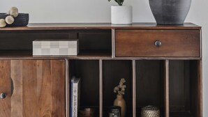 Een houten console tafel met een spiegel, een bloempot, een lamp en decoratieve objecten.