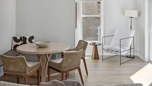 Een moderne eetruimte met een ronde tafel, rieten stoelen, een witte stoel en een vloerlamp.