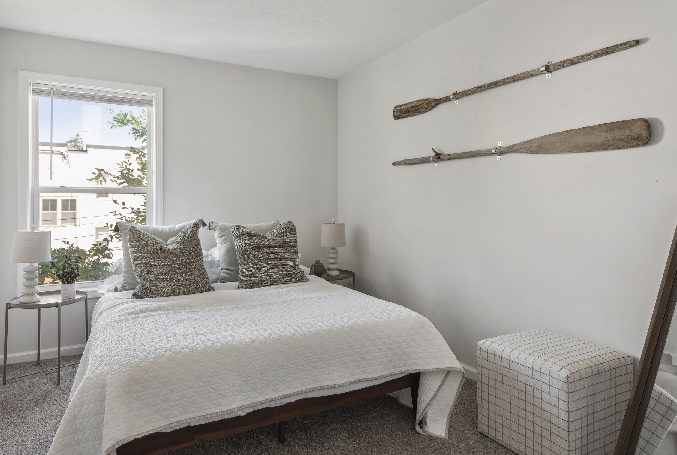 Une chambre à coucher avec un lit, des oreillers, une table de chevet, une lampe et une fenêtre donnant sur des immeubles.