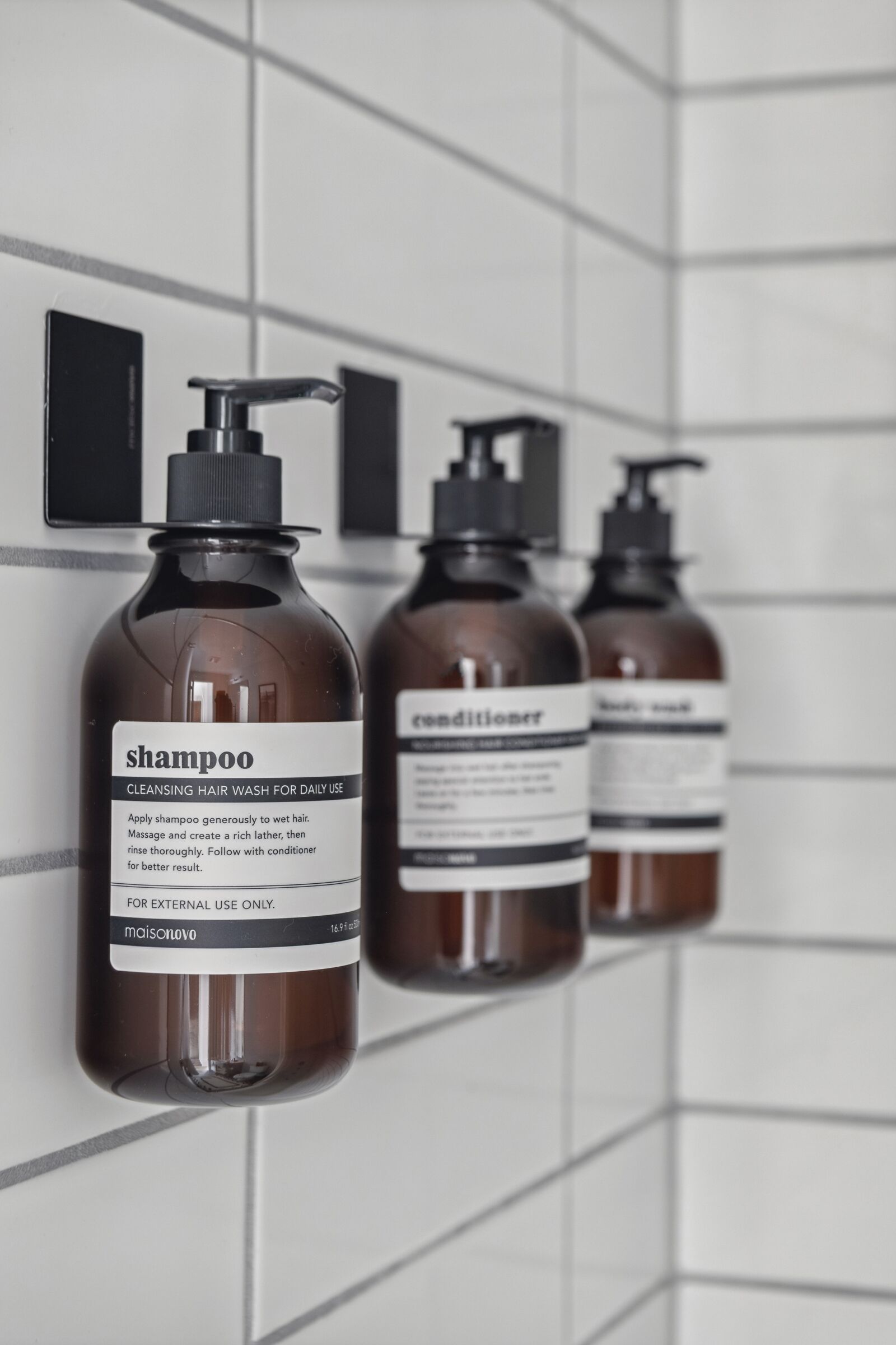 Three bottles of shampoo and conditioner mounted on a tiled wall.