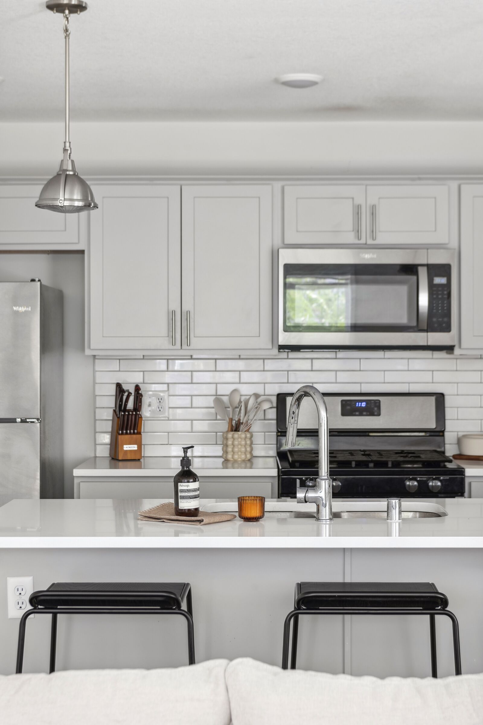 A modern kitchen with white cabinets, a stainless steel refrigerator, a microwave, and a sink with a faucet. There is a coffee maker and a knife block on the counter.