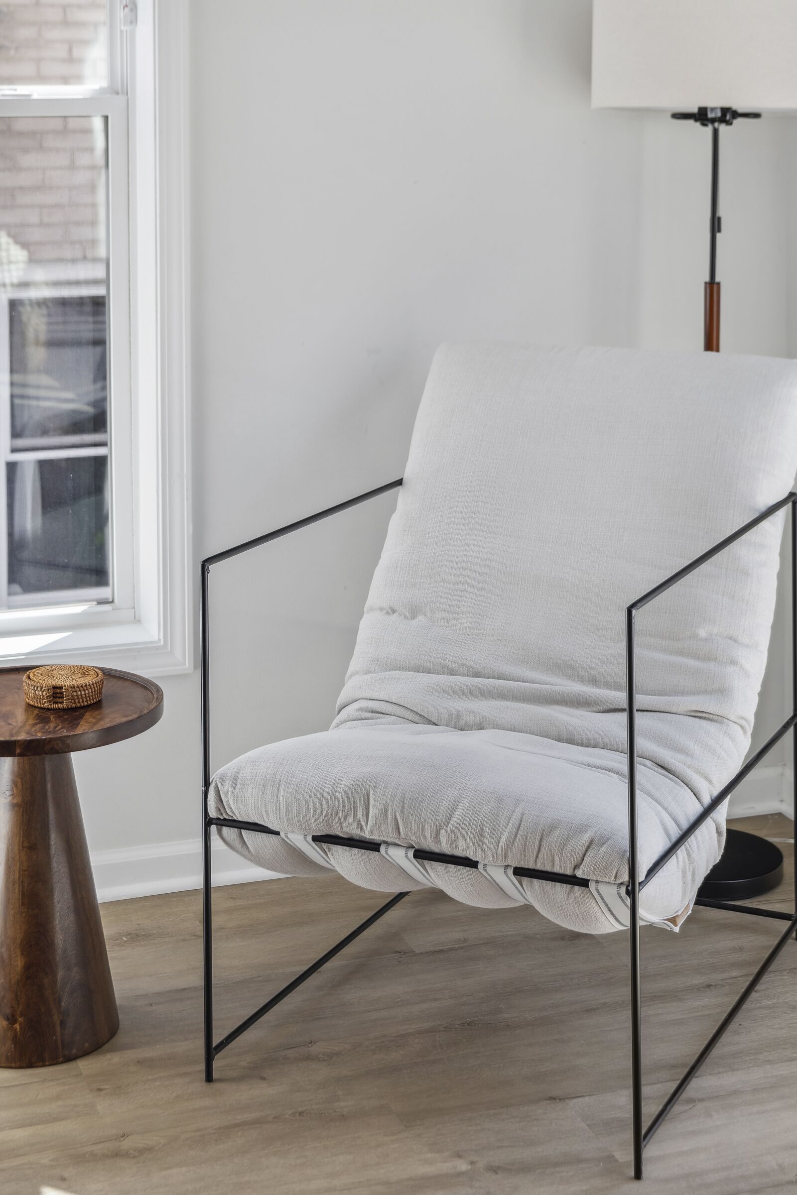 A modern chair with a metal frame and a light-colored cushion, positioned next to a round wooden table with a woven basket on it.