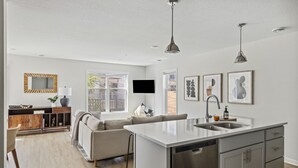 Een moderne keuken met een centraal kookeiland, roestvrijstalen apparatuur en een zithoek met een bank en bijzettafeltje.