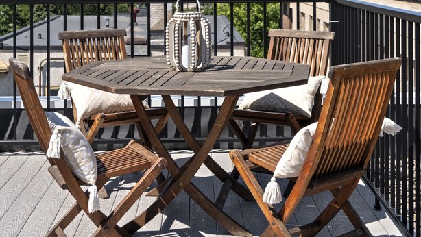 Een dakterras met een houten tafel en stoelen, sfeerverlichting en uitzicht op de stadsgezicht.