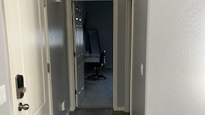 Un couloir avec une porte blanche sur la gauche, un mur blanc sur la droite et un sol carrelé.