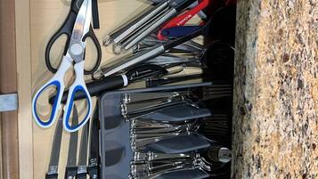 A drawer containing various kitchen utensils including scissors, tongs, and a grater.
