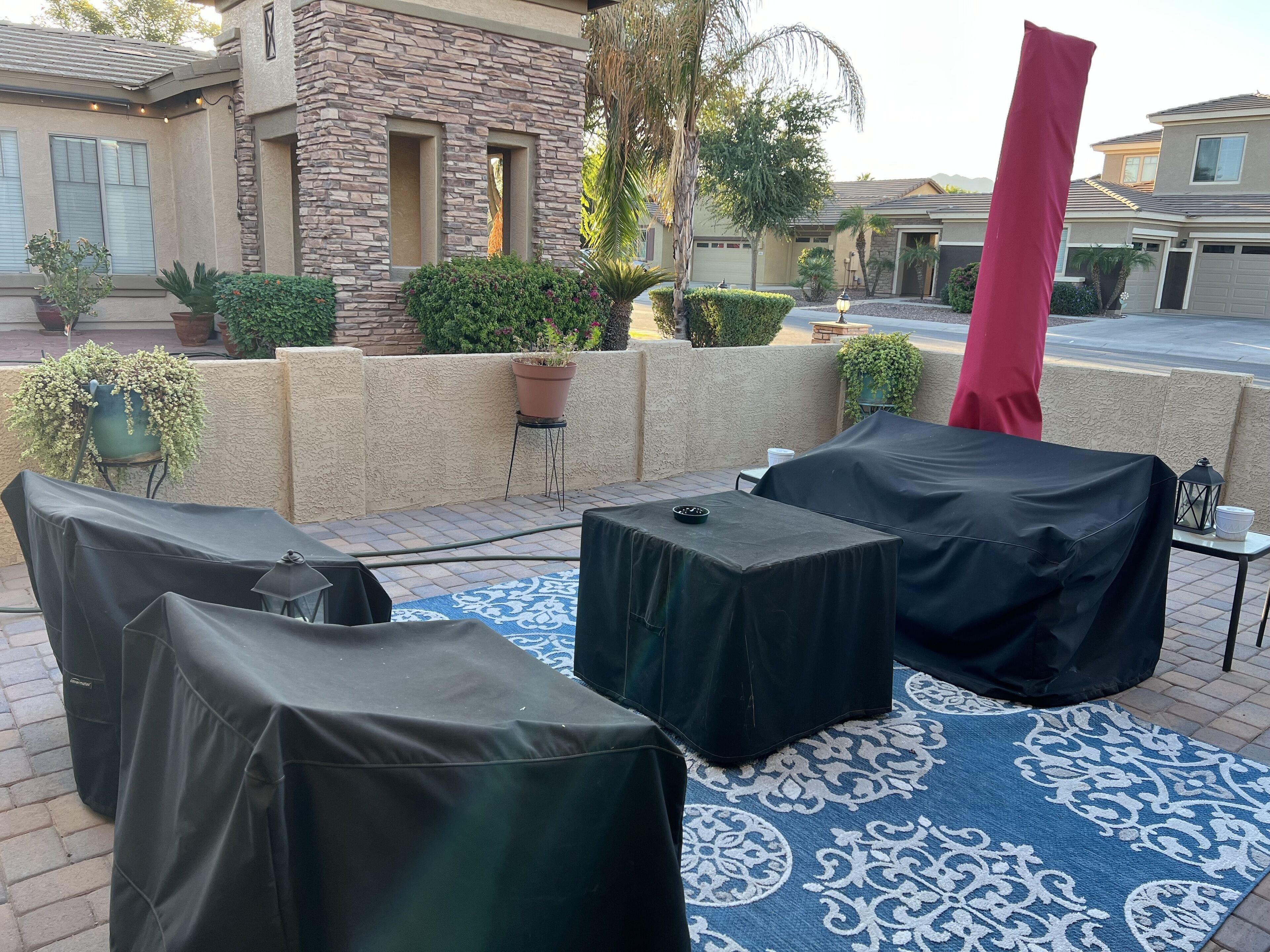 Une terrasse extérieure dotée d’un espace salon couvert, d’un tapis à motifs et de plantes en pot.