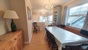 A spacious kitchen with a long dining table, wooden cabinets, and a window with a view of a bridge. - Large house (Norfolk) | Sleeps12 | 2min walk to beach | Dogs poss (2) | Playroom (SHERINGHAM)