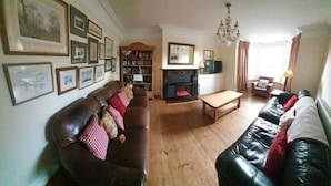 A living room with a fireplace, leather sofas, a coffee table, and a bookshelf. - Large house (Norfolk) | Sleeps12 | 2min walk to beach | Dogs poss (2) | Playroom (SHERINGHAM)