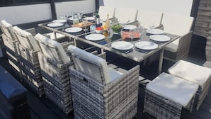 An outdoor dining area with a table set for four, surrounded by wicker chairs. - Large house (Norfolk) | Sleeps12 | 2min walk to beach | Dogs poss (2) | Playroom (SHERINGHAM)