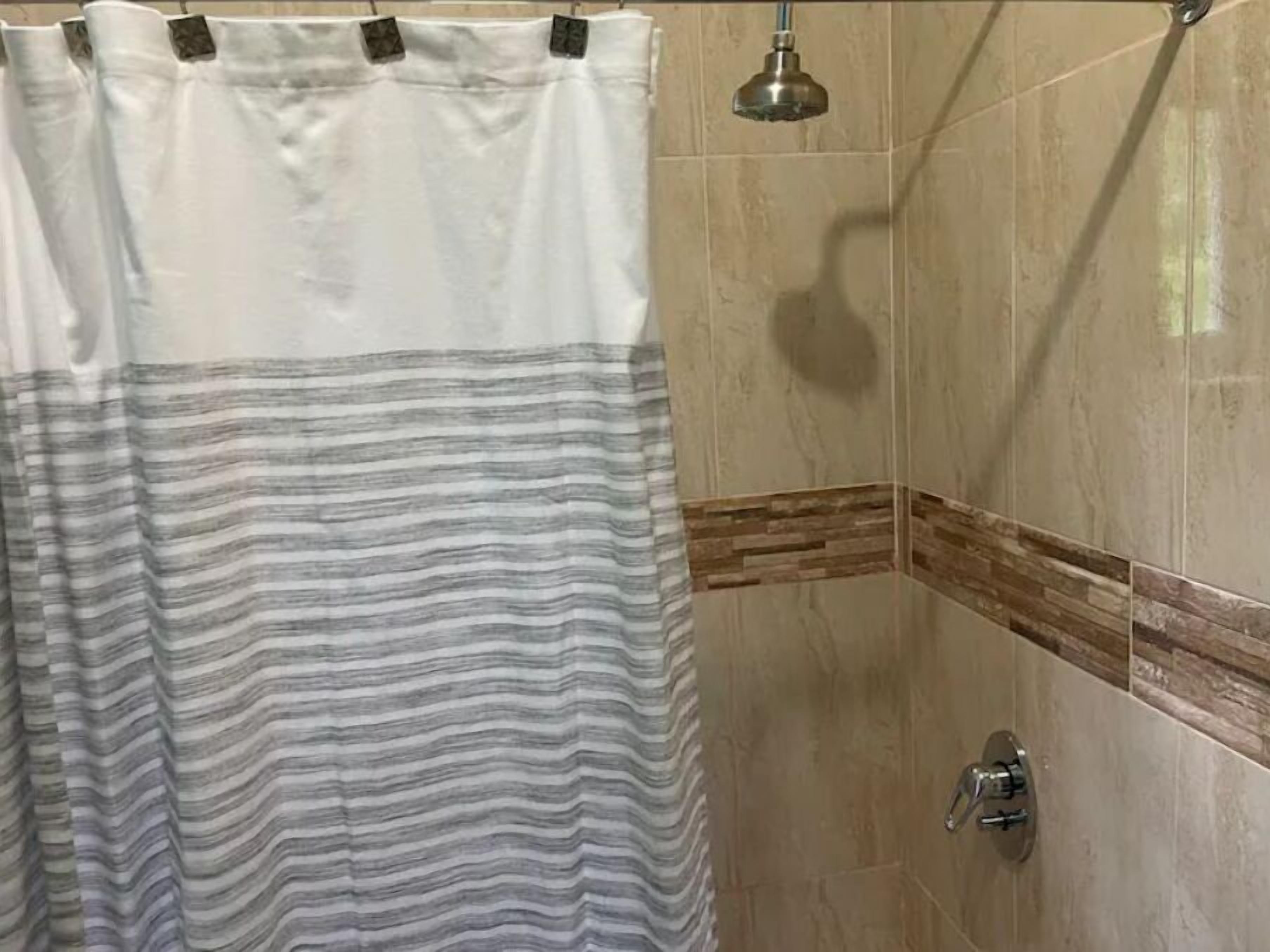 Un espace douche doté d’un rideau de douche à rayures, d’un pommeau de douche à main et d’un motif de carreaux décorant un coin.