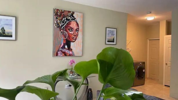 Een woonkamer met een groot schilderij, een plant en een wasruimte.