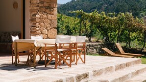 A building with a stone wall, a balcony with vertical slats, and a table with chairs outside. - Casa do Lagar by Quinta de Recião (Lamego)